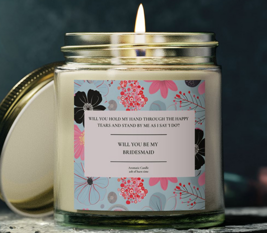 Candle with a floral label asking 'Will you be my bridesmaid?' on a dark background