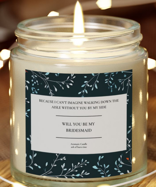 Candle in a jar with a label asking 'Will you be my bridesmaid?' on a wooden surface.