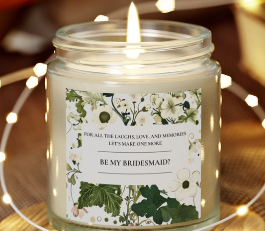 Candle in a jar with a floral label asking 'Be My Bridesmaid?' on a wooden surface with string lights.