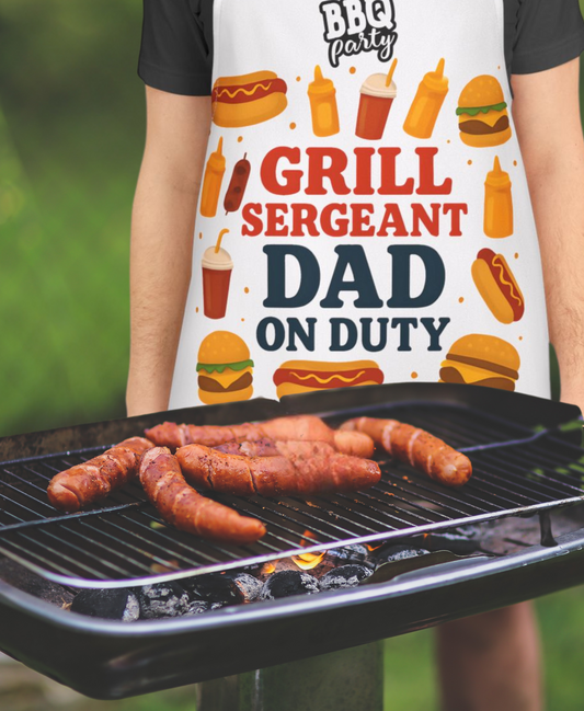 Person grilling hot dogs wearing a 'Grill Sergeant Dad on Duty' apron with BBQ-themed graphics.